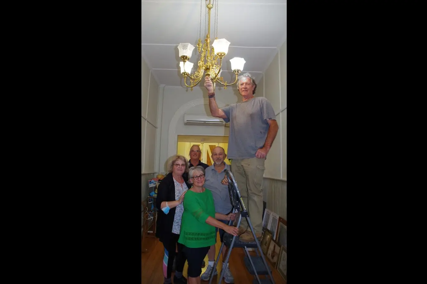 FINISHING TOUCHES:  Nagambie Mechanics Hall volunteers watch Ian Barford as he installs the bargain chandelier in the foyer. The day before the Op Shop re-opening. Supporting the ladder are Peter Branagan, Hugh Lawrence, Jackie Berry and June De Bono. 